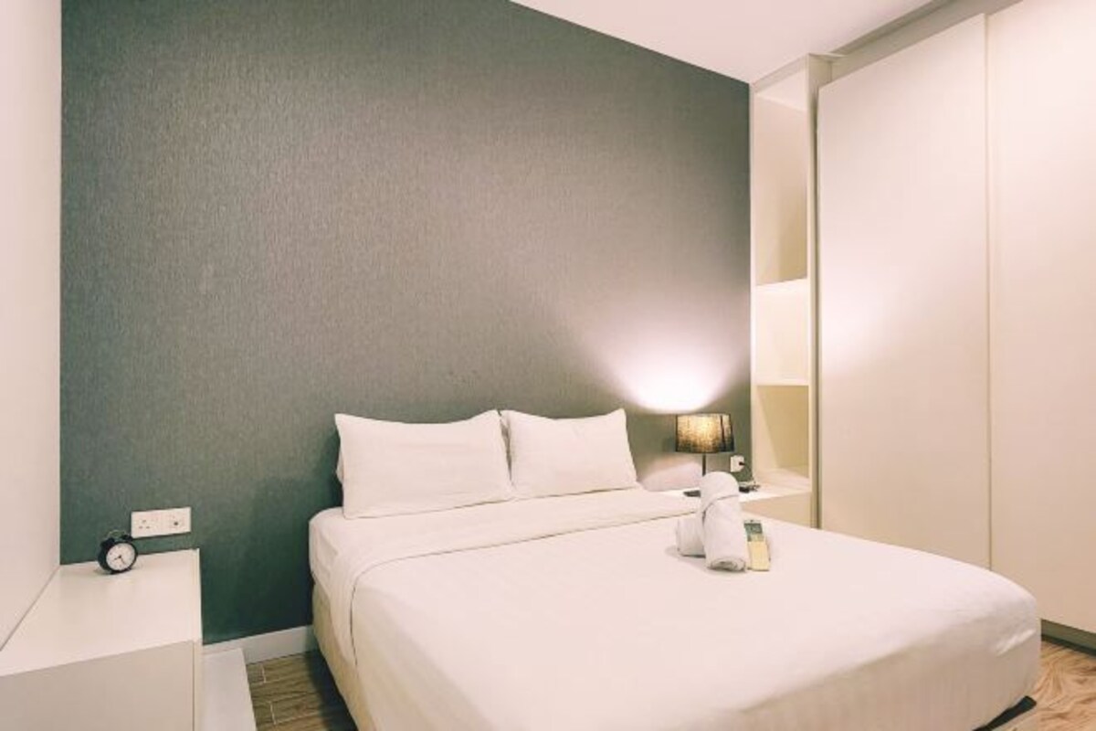 Een net opgemaakt bed met kussens, een nachtkastje met een lamp en een wekker.