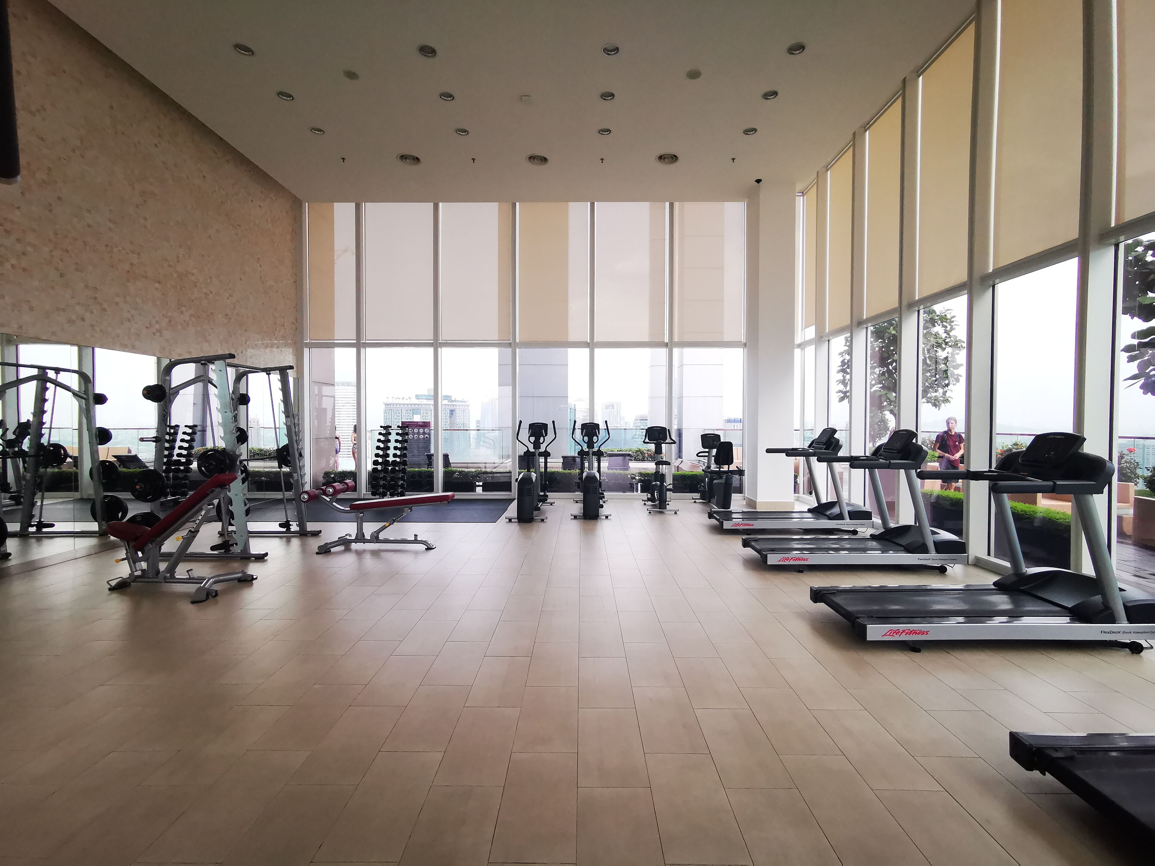 Een ruime fitnessruimte met grote ramen, diverse fitnessapparaten en uitzicht op de stad.