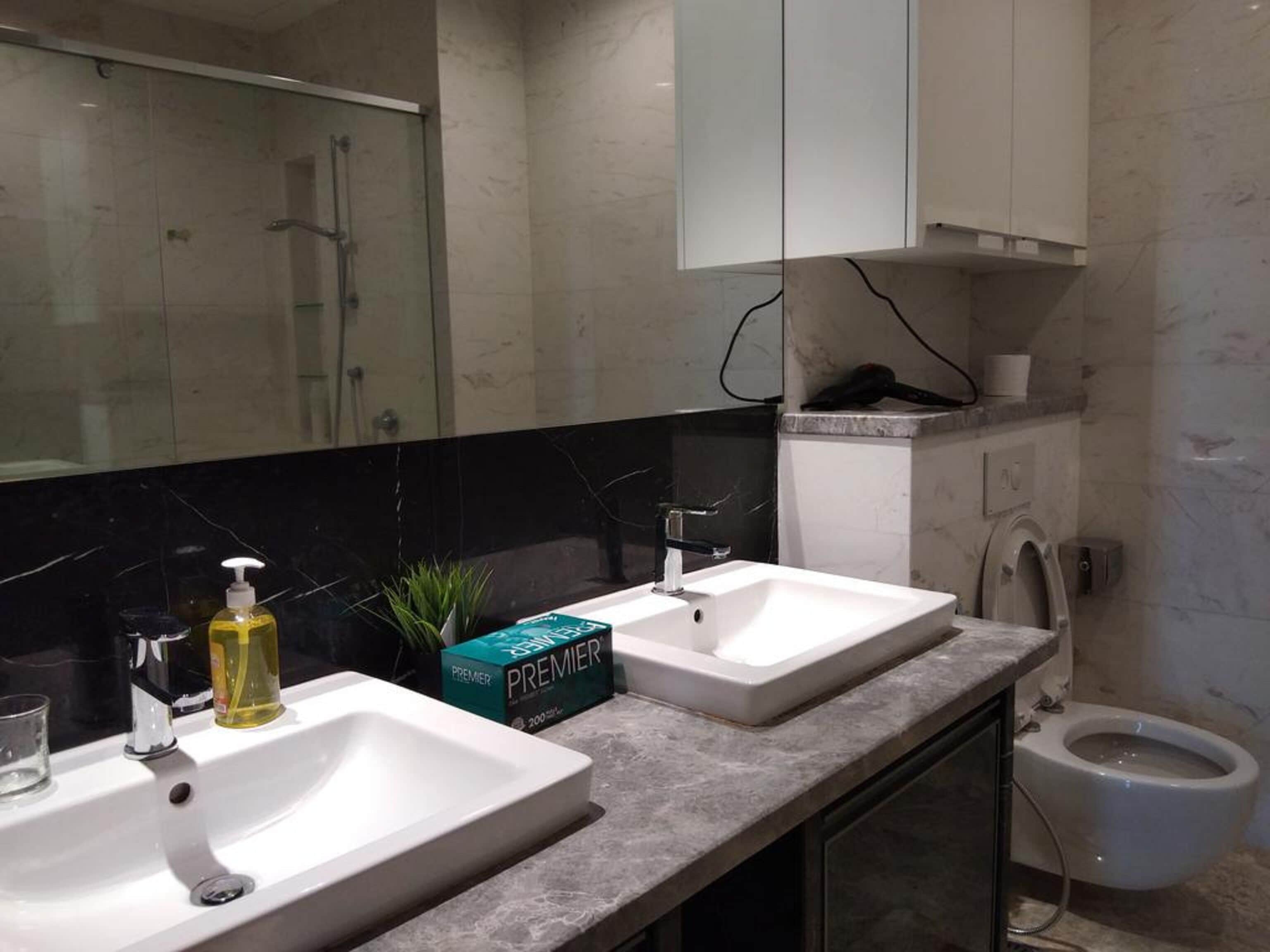 A modern bathroom with two sinks, a shower, and a toilet.