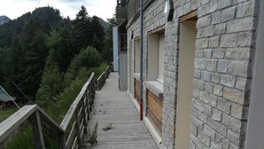 Una terraza de madera que conduce a un edificio de piedra con múltiples ventanas y un balcón.