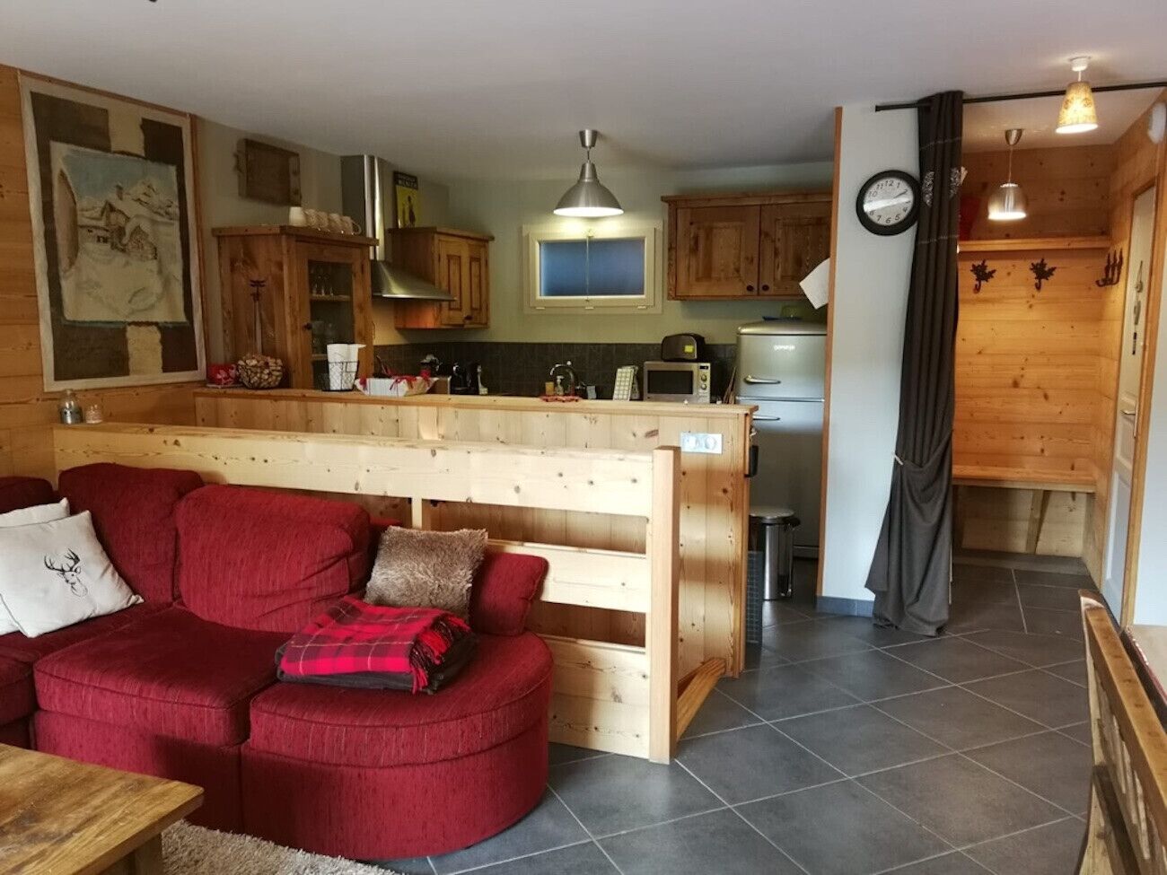 Un salon confortable avec un canapé rouge, des meubles en bois et un coin cuisine équipé d’un four à micro-ondes et d’un grille-pain.