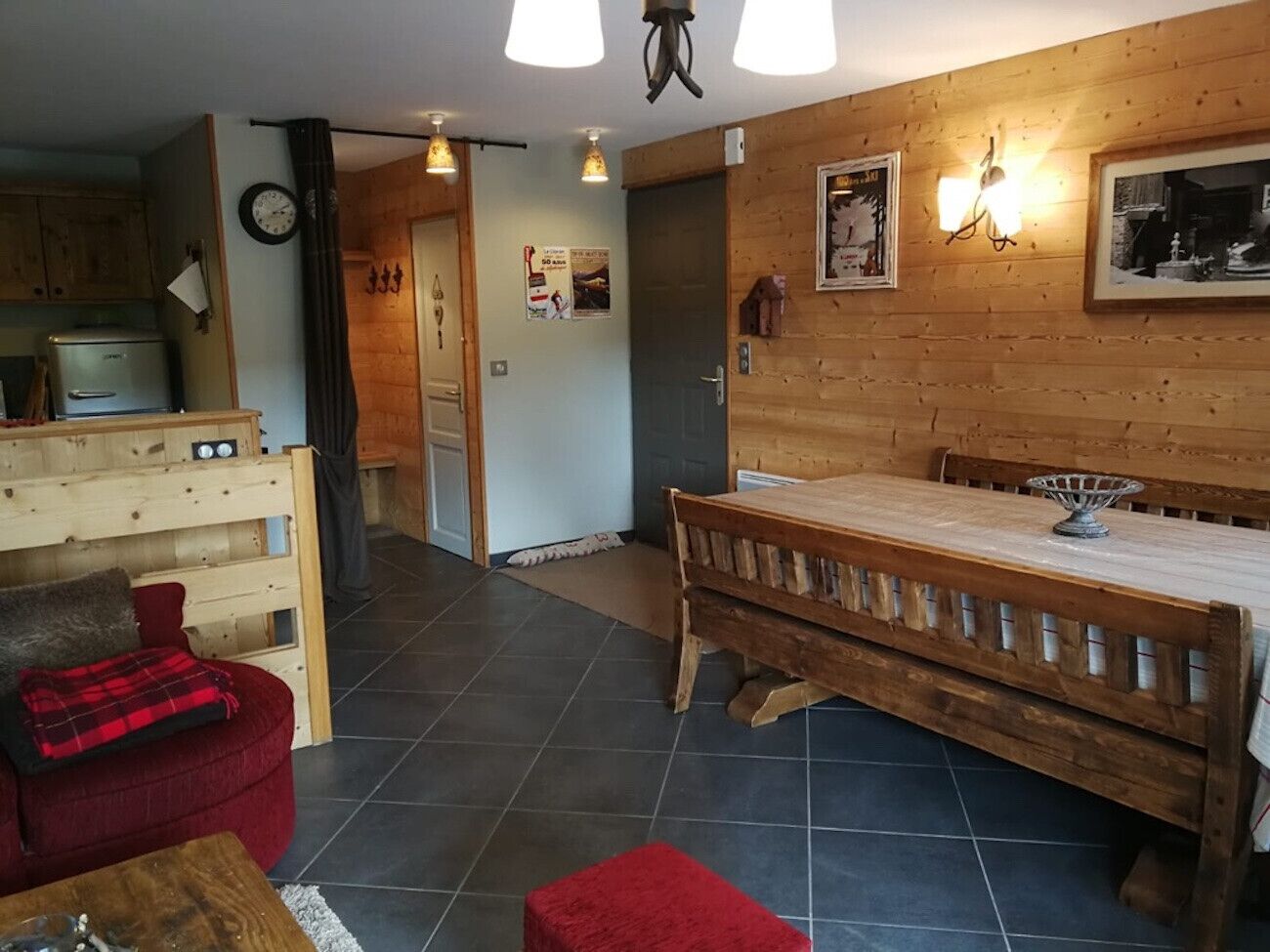 A cozy room with a wooden bed, a red sofa, and a small table. There is a kitchen area with a refrigerator and a stove.