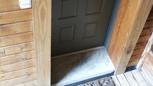 Una puerta de madera con una placa que indica la habitación 12, un pequeño escalón que lleva a la puerta y una pared de madera con diseño de panel horizontal.