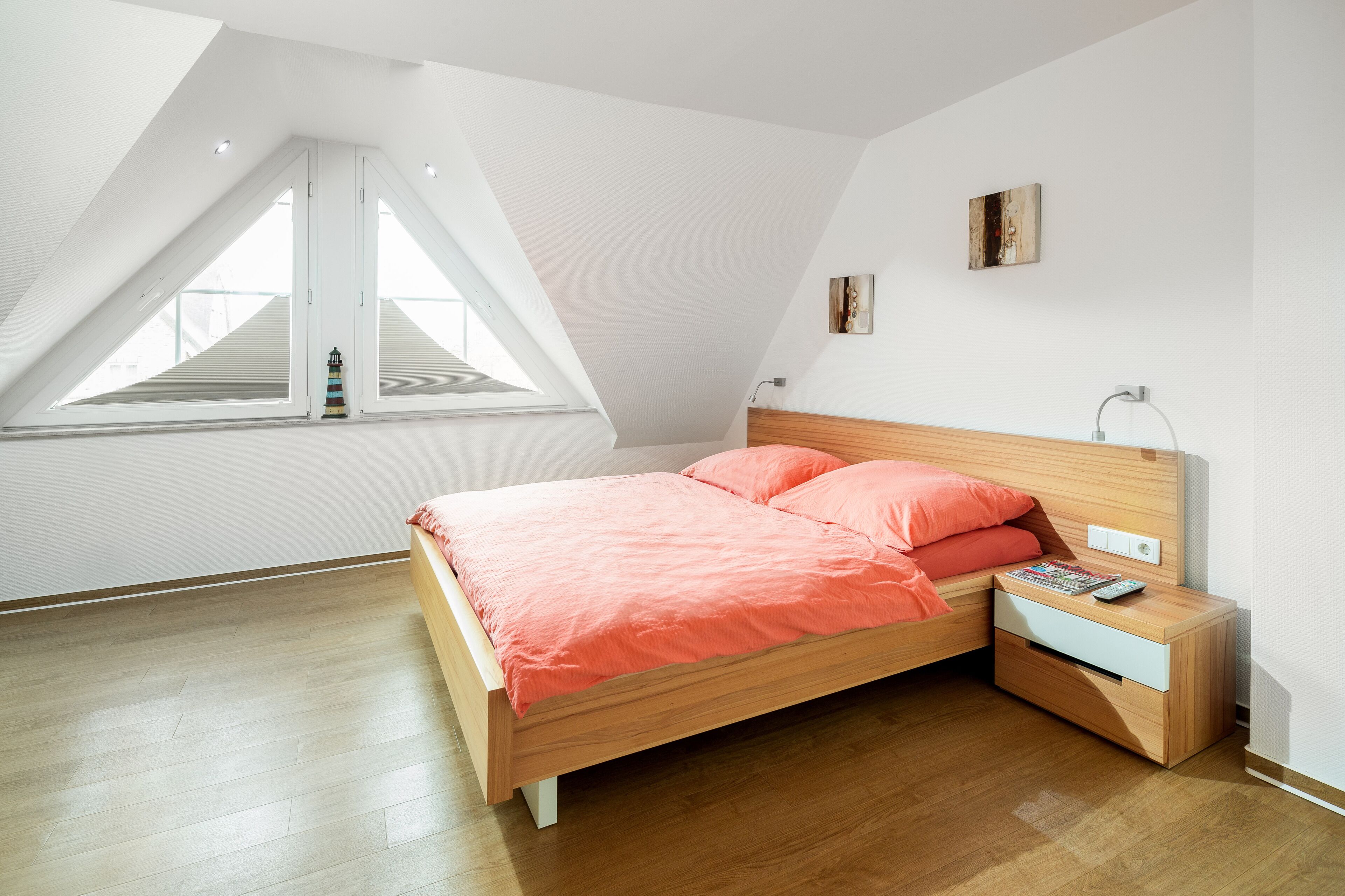 Une chambre avec un plafond en pente, un lit doté d’une tête de lit en bois, une table de chevet avec une lampe et une fenêtre offrant une vue.