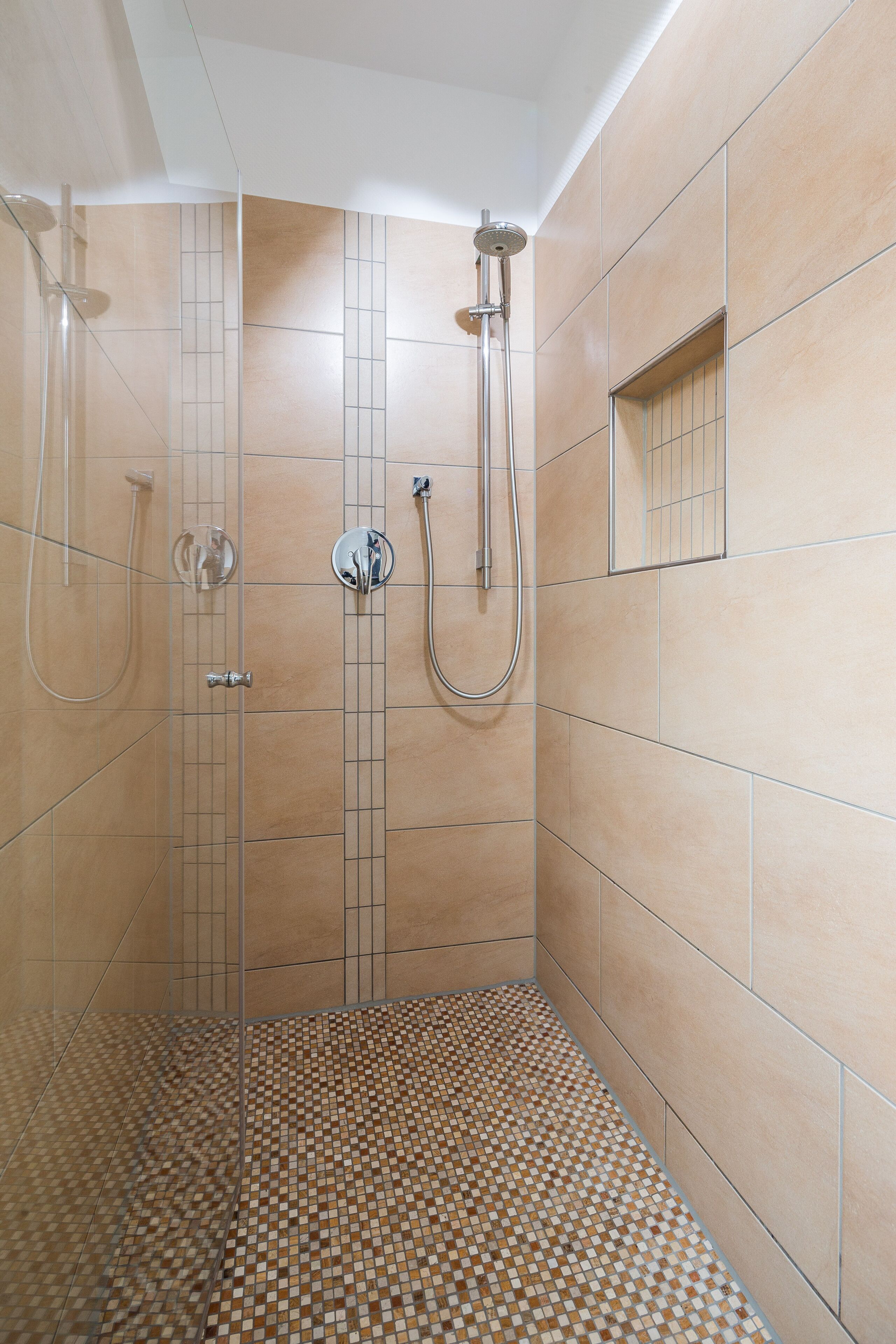 Une douche avec un sol et des murs carrelés, une douchette à main et un robinet fixé au mur.