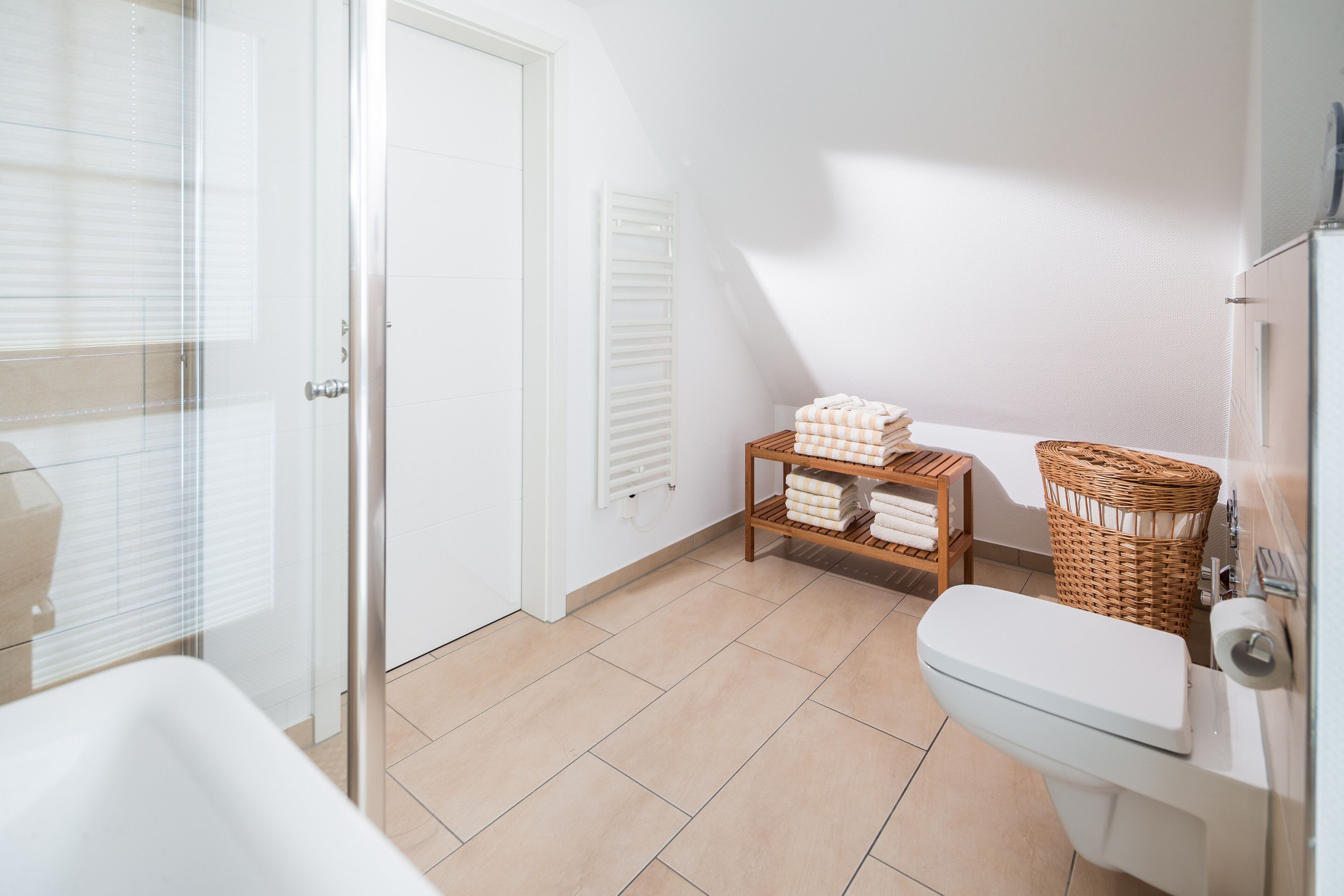 Une salle de bain comprenant des toilettes, un lavabo, une douche en verre, un panier en osier et une étagère avec des serviettes.