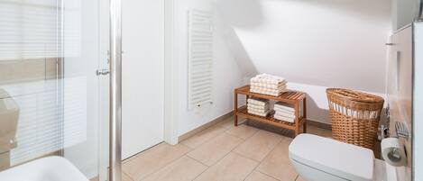 Une salle de bain comprenant des toilettes, un lavabo, une douche en verre, un panier en osier et une étagère avec des serviettes.