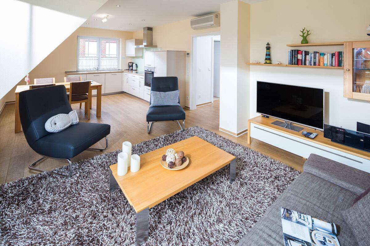 A modern living room with a sofa, a coffee table, a TV, and a bookshelf.