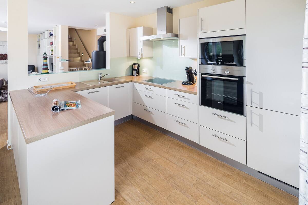 A modern kitchen with white cabinetry, a built-in oven, and a wooden countertop.