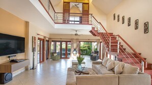 A spacious living area with a large flat-screen TV, a comfortable sofa, a glass coffee table, and a staircase leading to an upper level. - Blissful Villa Felicity with Ample Space (Rawai)