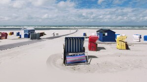 A beach with a row of beach huts and a striped beach chair. - Winkelschiffchen II (Juist)