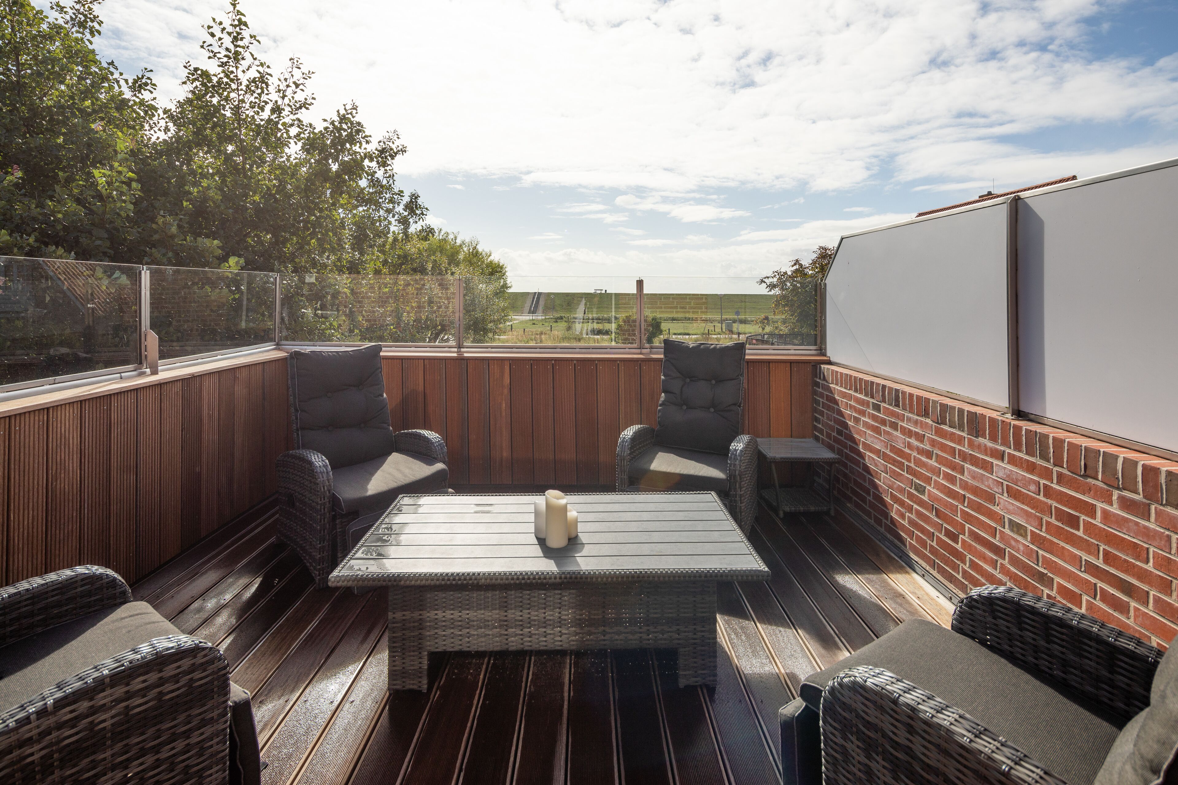 En udendørs terrasse med fletmøbler, et bord og udsigt over landskabet.