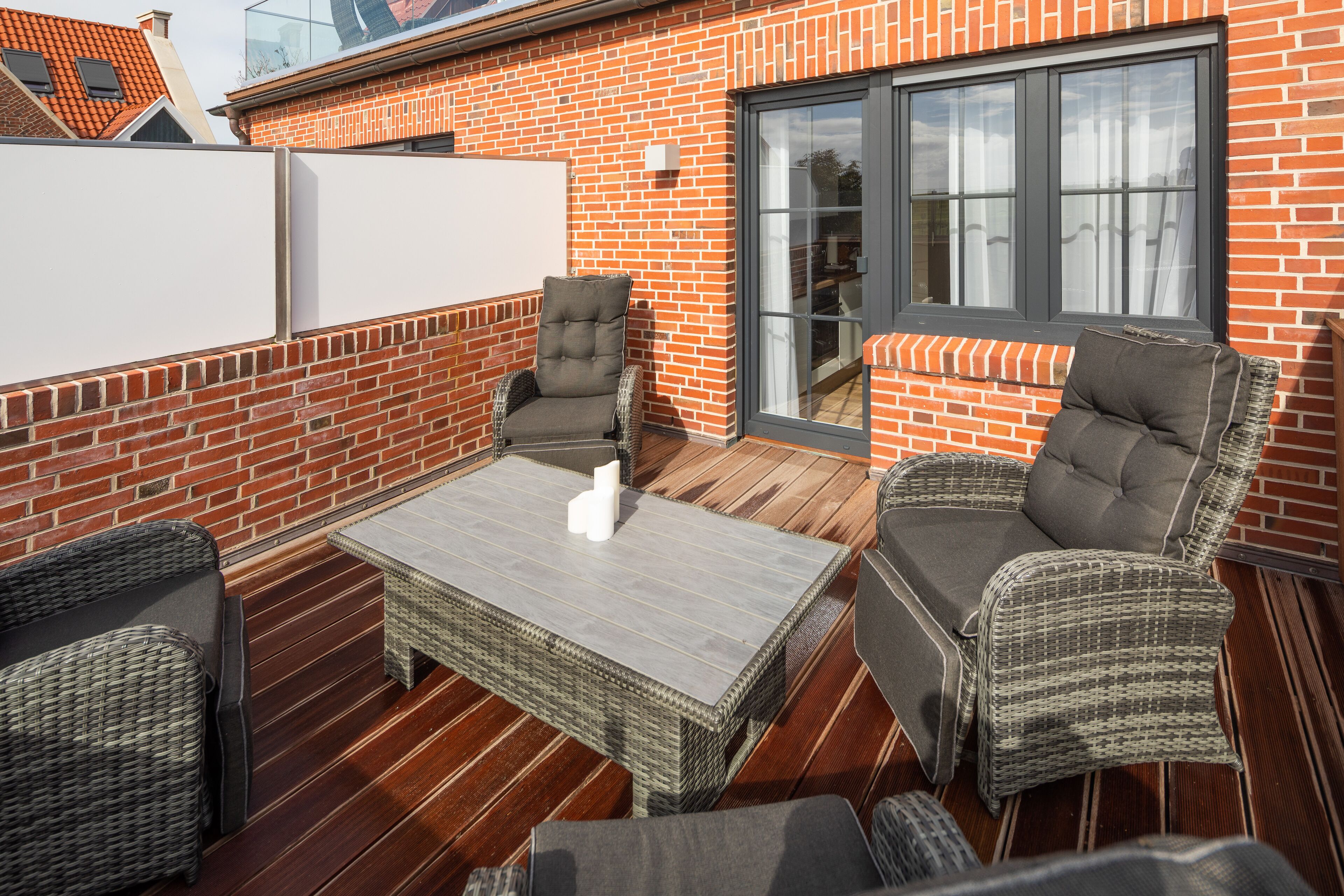 Eine Dachterrasse mit Korbmöbeln, einer Glastür und einer Ziegelwand.