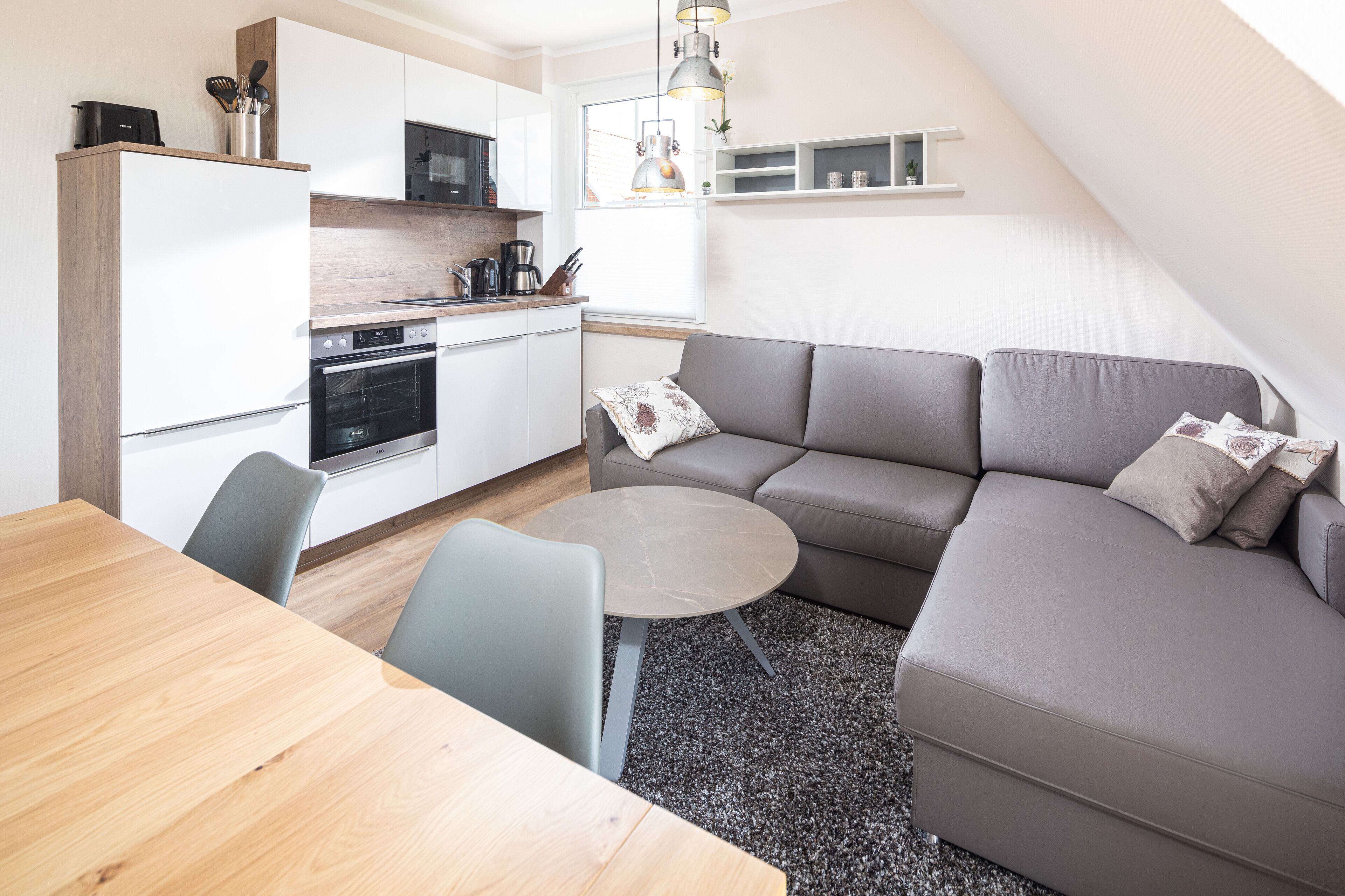 Eine moderne Küche mit weißen Schränken, einem Esstisch und einem grauen Sofa.