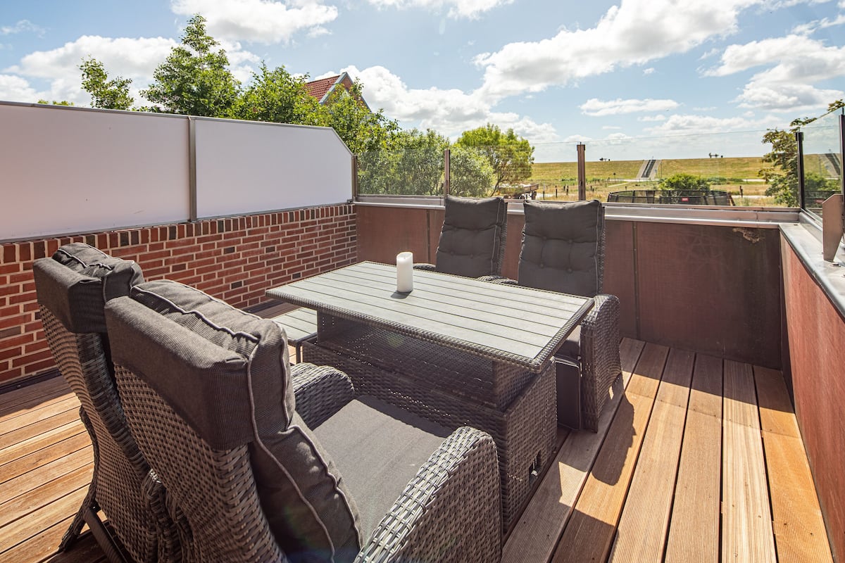 An outdoor patio with wicker furniture, a wooden table, and a view of the countryside.