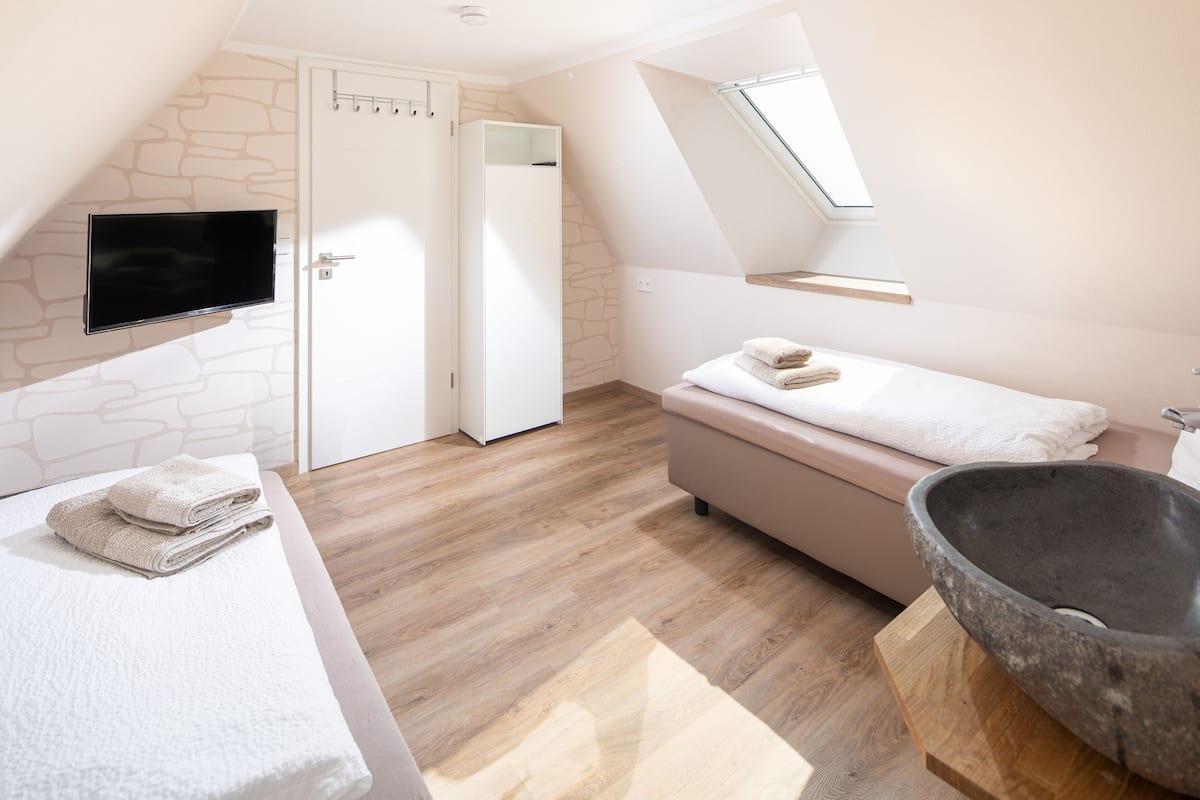 A modern bedroom with a stone wall, a flat-screen TV, a bed with a wooden headboard, a stone sink, and a skylight.