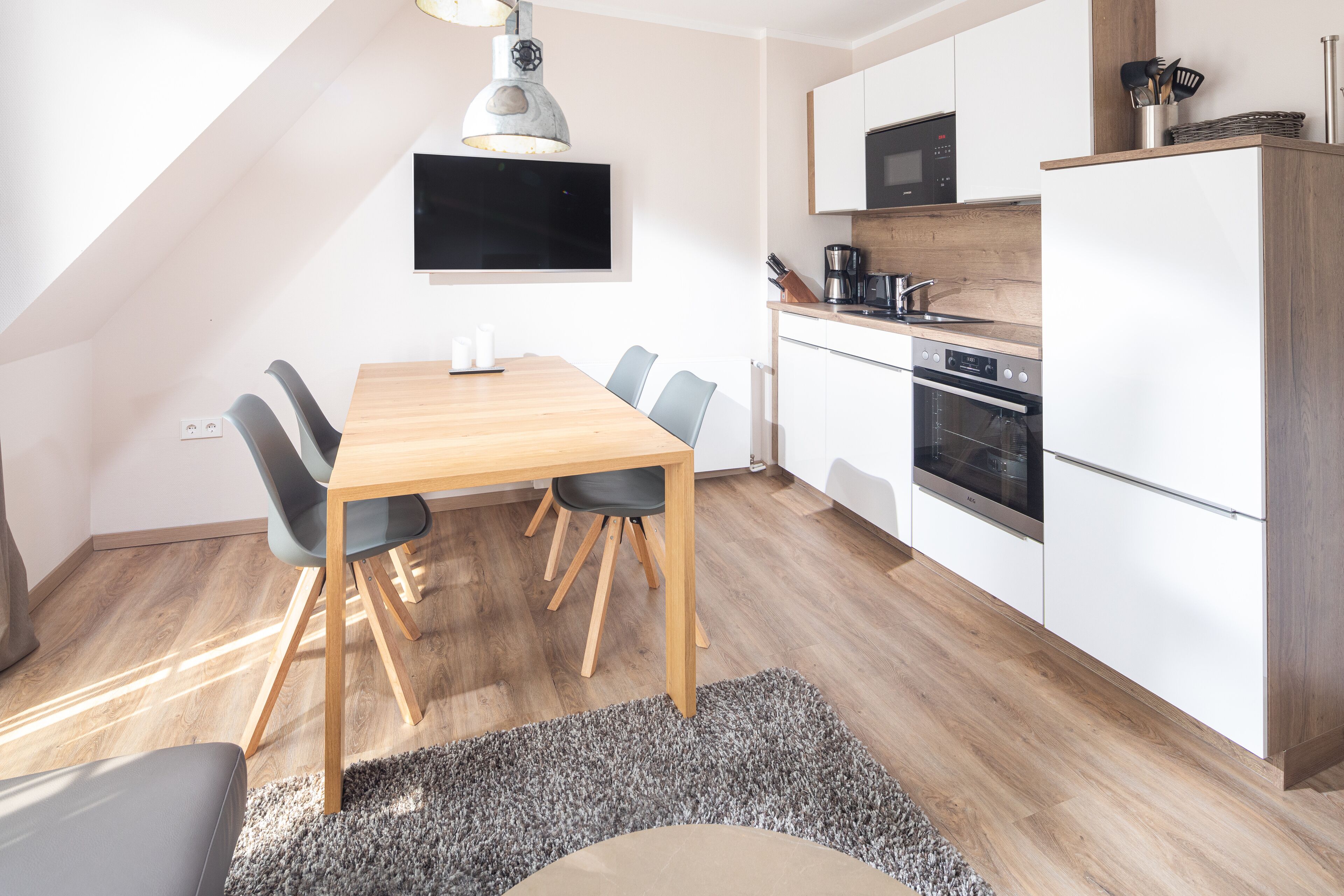 A modern kitchen with white cabinets, a wooden dining table, and a gray rug.