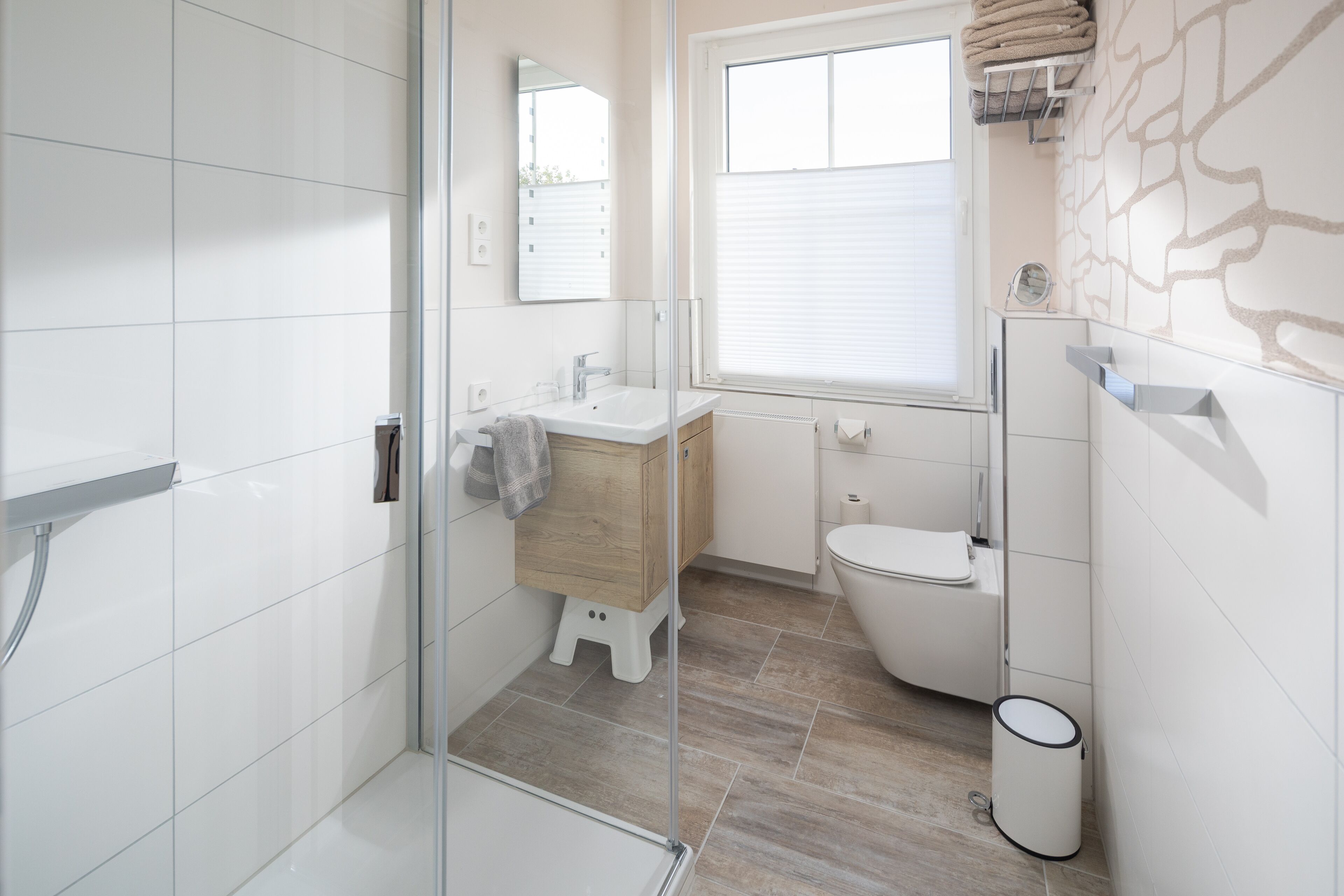 Une salle de bain moderne avec une douche à parois de verre, un meuble-lavabo en bois, un lavabo blanc et des toilettes.