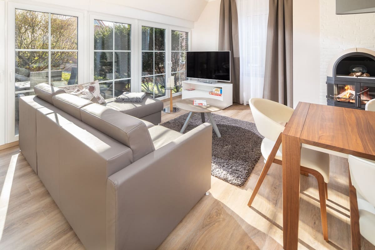A modern living room with a large window, a flat-screen TV, a fireplace, and a dining area.
