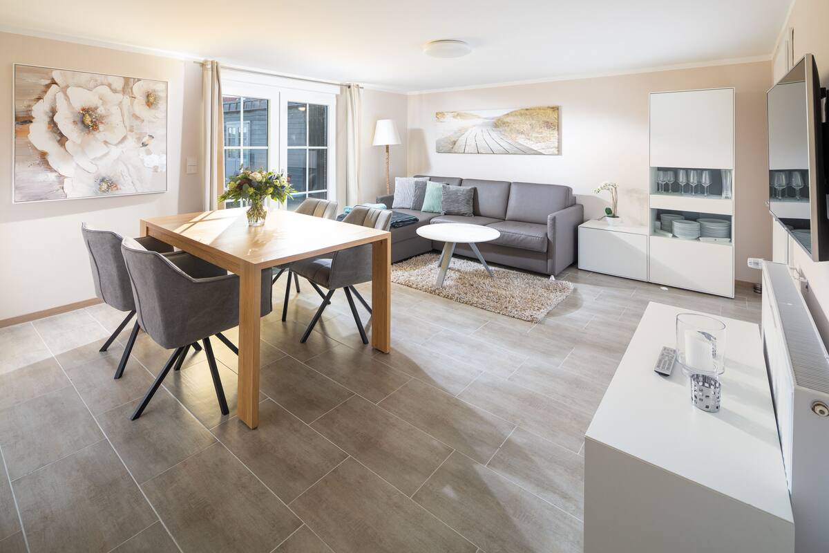 A modern living room with a dining area, a sofa, a coffee table, and a TV stand.