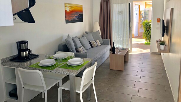 A modern living room with a dining area, a grey sofa, a coffee machine, and a painting on the wall. - Los Leones Bungalows (San Bartolomé de Tirajana)