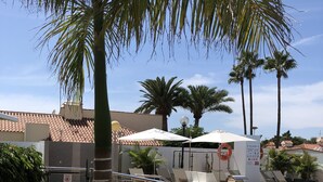 A pool area with a tiled deck, palm trees, lounge chairs, and a lifebuoy. - Los Leones Bungalows (San Bartolomé de Tirajana)