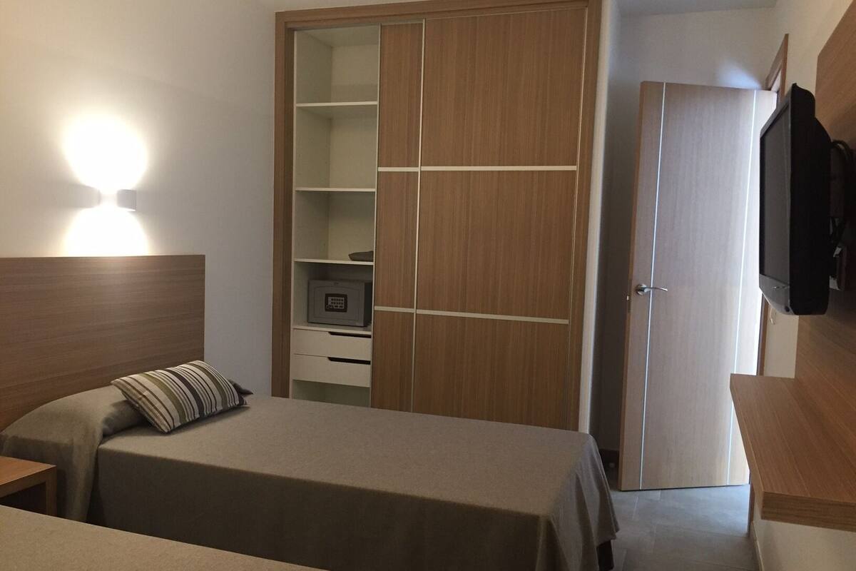 A bedroom with two beds, a wardrobe, a desk, and a television.