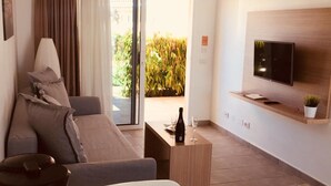 A modern living room with a sofa, a coffee table, a TV mounted on the wall, and a view of the outdoors. - Los Leones Bungalows (San Bartolomé de Tirajana)