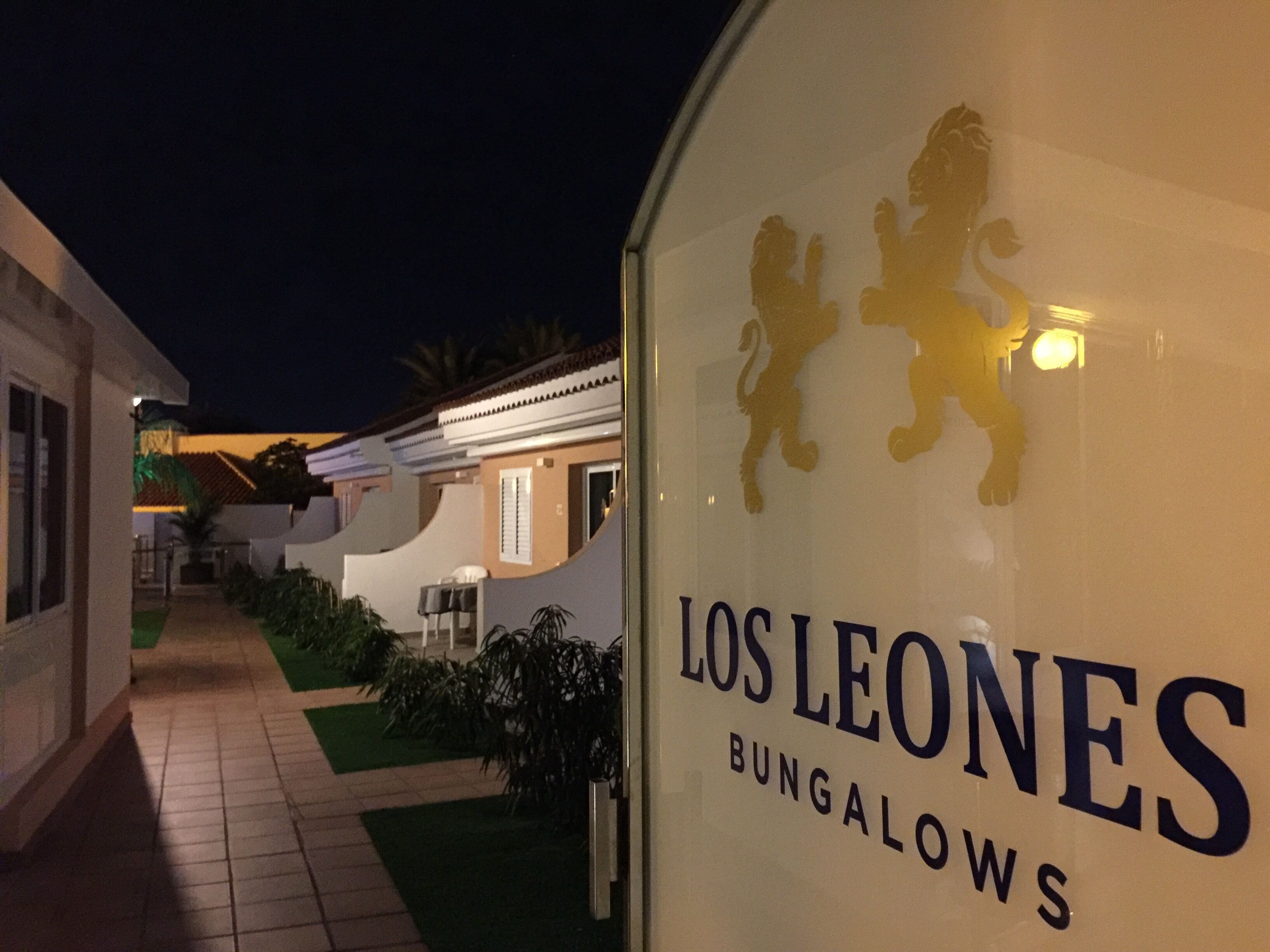 A sign for "Los Leones Bungalows" with a lion silhouette and a pathway leading to a building.