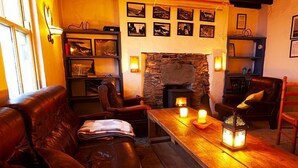 A cozy living room with a fireplace, leather sofa, wooden table, and wall-mounted shelves. - Great Blasket Island Accommodation (Great Blasket)
