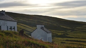A white building with the word "CAFE" on its side, set against a backdrop of rolling hills and a cloudy sky. - Great Blasket Island Accommodation (Great Blasket)