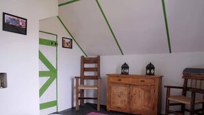 A room with a bed, a wooden cabinet, two chairs, and a door with green accents. - Great Blasket Island Accommodation (Great Blasket)