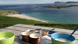 A table with bowls and a plate of food, overlooking a beach and ocean. - Great Blasket Island Accommodation (Great Blasket)
