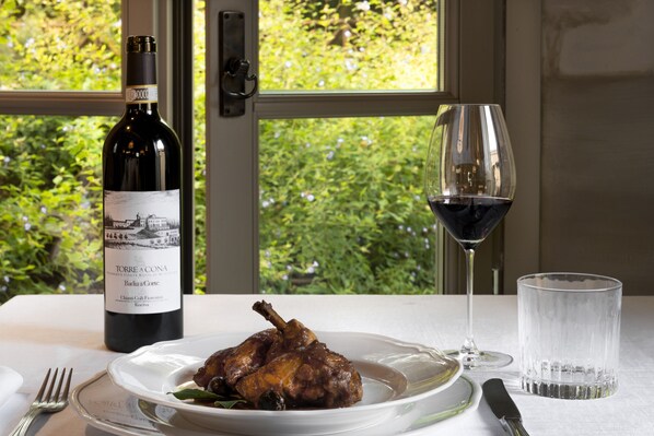 Una mesa de comedor con una botella de vino, una copa de vino tinto, un plato de comida y cubiertos.