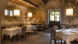 Un espace repas avec des tables préparées pour deux personnes, doté d’un plafond rustique et offrant une vue sur l’extérieur grâce à une porte.