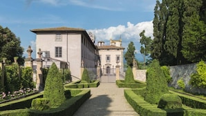 Un jardin à la française qui mène à un bâtiment de style classique, avec un aménagement paysager symétrique et un ciel dégagé.