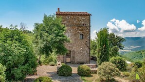 A stone tower with a door, surrounded by greenery and a mountainous backdrop.
