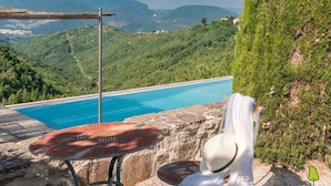 A pool with a view of mountains, a chair, and a hat on a table.