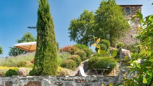 A stone wall, a tall coniferous tree, and a stone building with a tiled roof.
