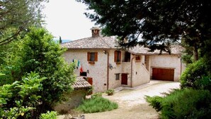 Une maison de campagne en pierre, avec un toit en tuiles, un petit jardin et un garage.