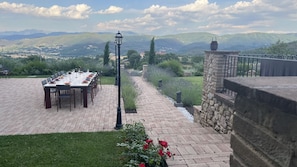 A patio with a long dining table, a lamp post, and a stone wall.