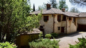 A rustic stone building with a tiled roof, a paved courtyard, and surrounding greenery.