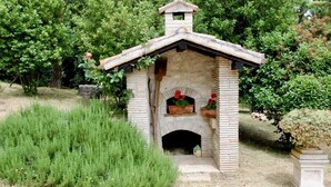 Une cheminée extérieure en pierre, avec un conduit en briques, entourée d’une végétation luxuriante.