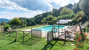 A rectangular pool with a wooden fence, outdoor seating, and umbrellas. - Villa con Piscina - Villa La Ginestra (Umbertide)