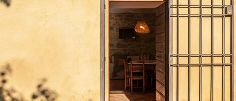 An open doorway leading to a room with a stone wall, a wooden table, chairs, and a hanging light fixture.