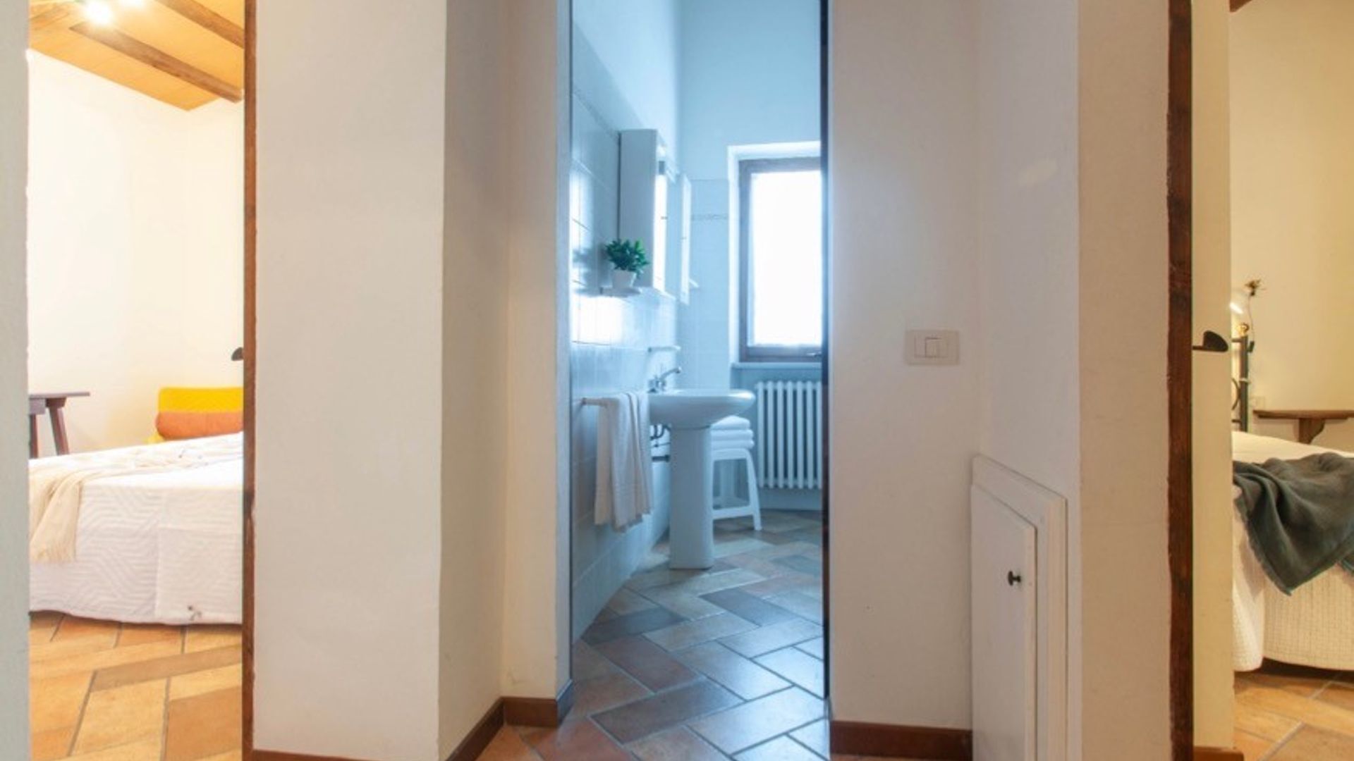 A hallway leading to a bathroom with a sink, a window, and a radiator.
