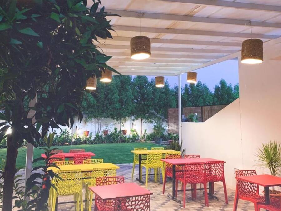 Un área de patio al aire libre con mesas y sillas, rodeada de vegetación y vista a árboles.