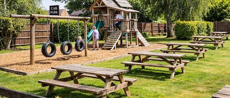A playground with swings, a slide, and picnic tables.