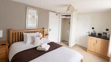 Quarto com uma cama grande, cabeceira de madeira, mesa de cabeceira, roupeiro e uma pequena área de cozinha.