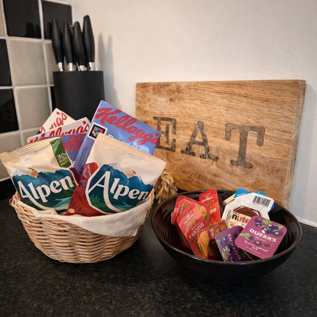 En køkkenbordplade med en kurv med snacks, en skål med pakket mad og et træskilt med ordet "EAT".